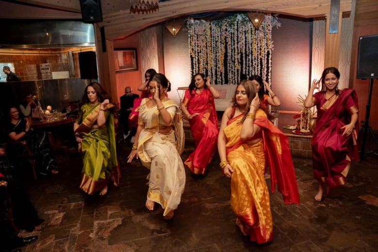 A group of women in colourful Indian dresses dance.