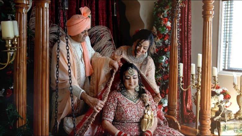 A woman in jewels is covered by a man with a turban and a woman.