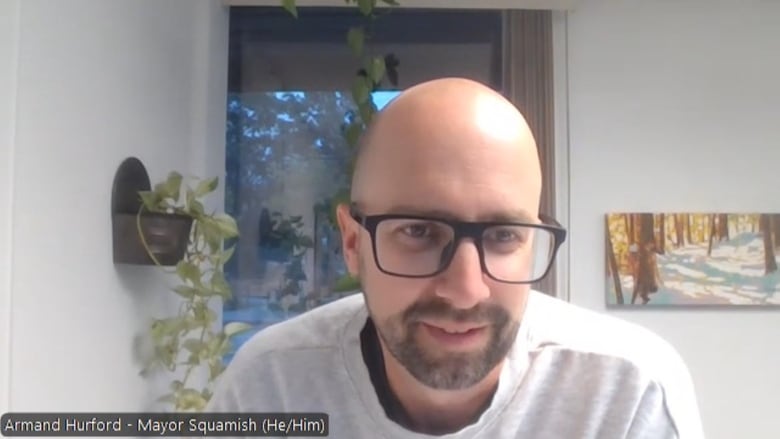 A man with glasses wearing a grey t-shirt looking at the camera. 