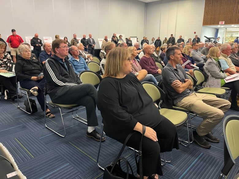 A large group of people sit listening to a public speaker.