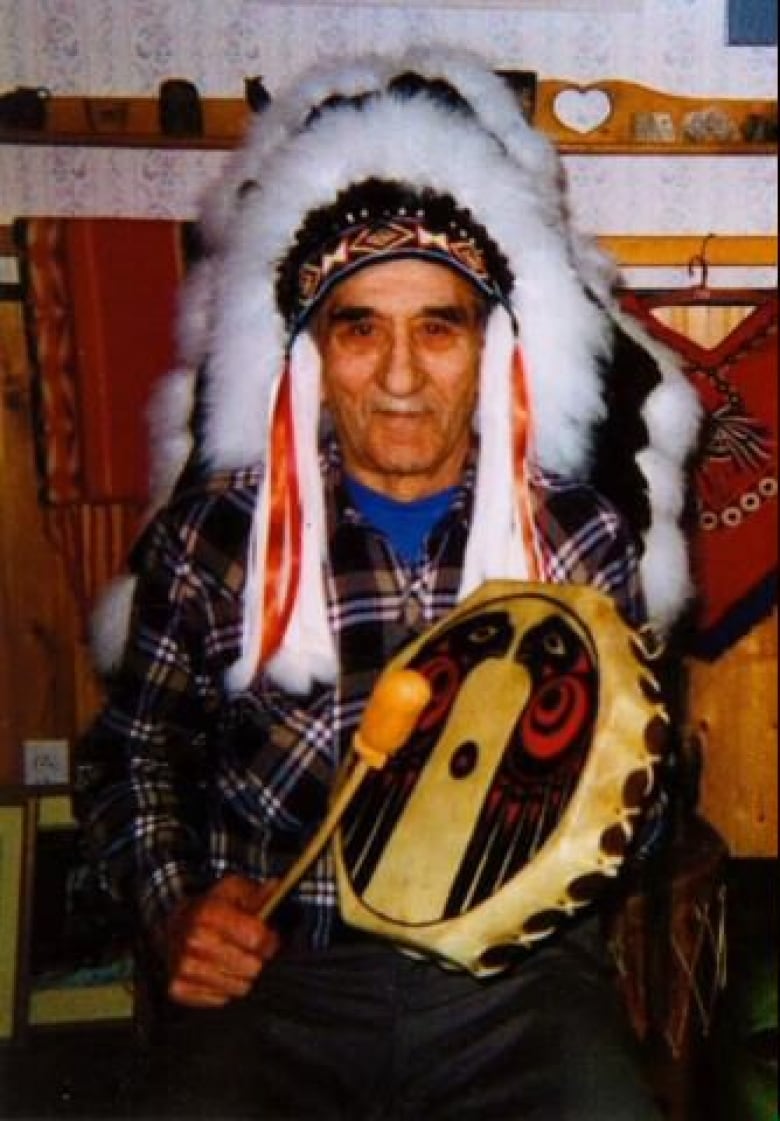 An older man wearing an Indigenous headdress and holding drums.