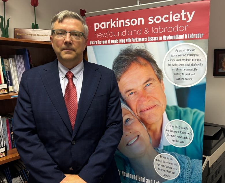 A person wearing a blazer and tie stands in front of a sign for the Parkinson's Society of Newfoundland and Labrador.