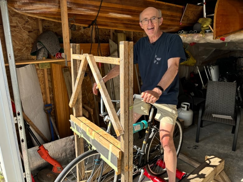 A person stands on a bicycle which sits on rollers and is surrounded by a wooded stand.