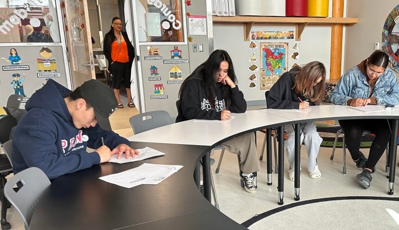 Four high school students write essays in a classroom