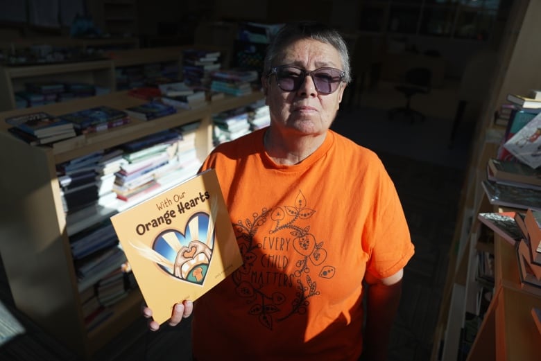 A woman wearing an orange shirt holds up a book titled 'With Our Orange Hearts.'