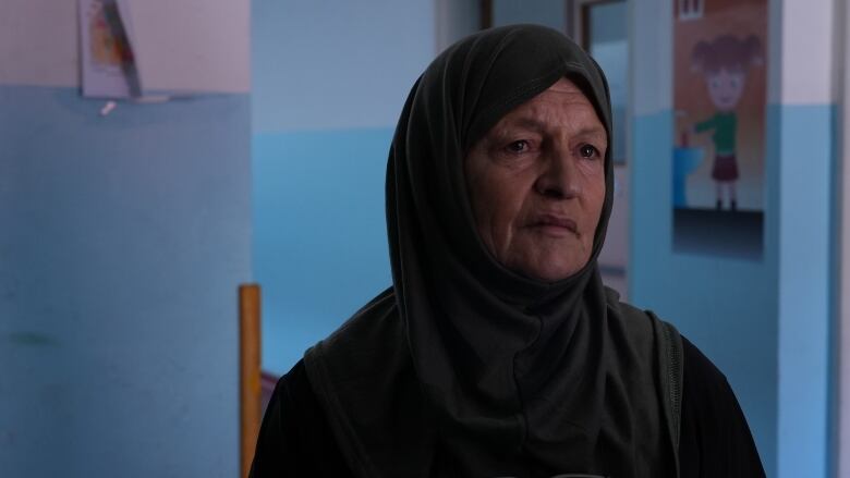 A woman wearing black tears up as she sits for an interview inside a house with blue walls.