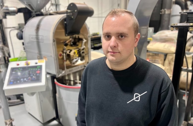 A man wearing a black sweatshirt stands in front of coffee machinery. 