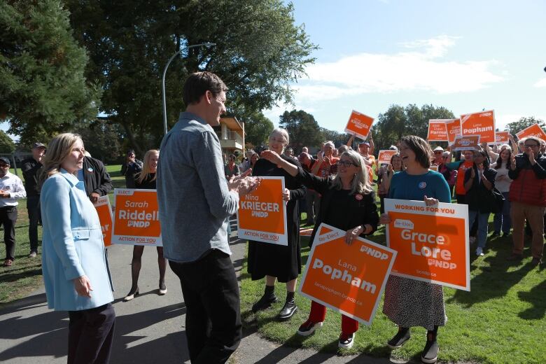 British Columbia NDP Leader David Eby faces supporters holding orange signs in an park.