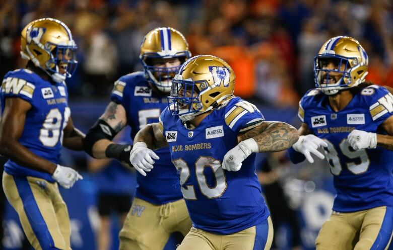 Four smiling football players in blue jerseys celebrate.