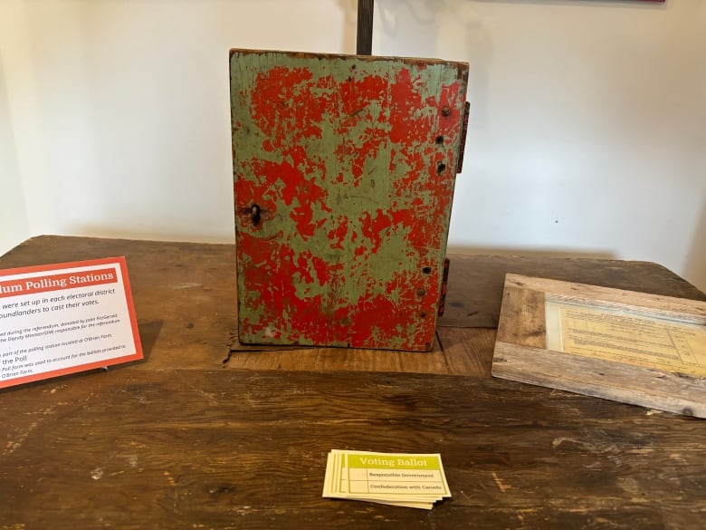 A close up of a box painted red but it's chipped away over time. On the table is a stack of voting ballot cards.