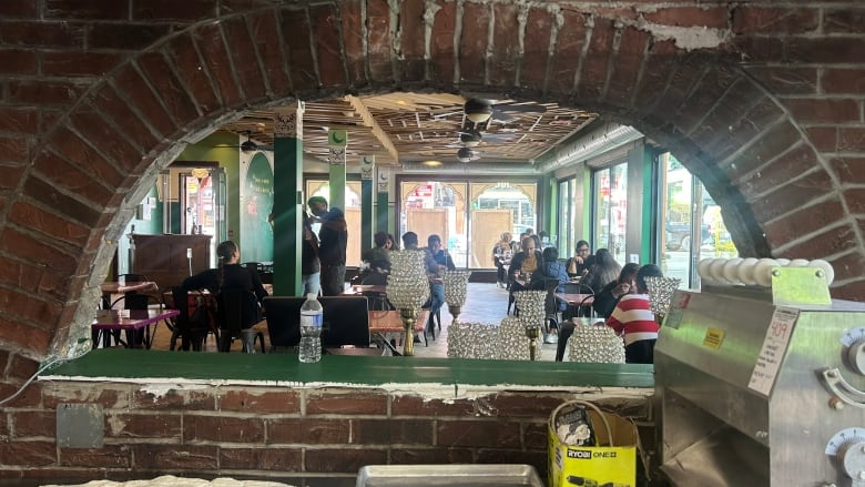 Through a large hole in a brick wall, a restaurant is seen packed with customers.