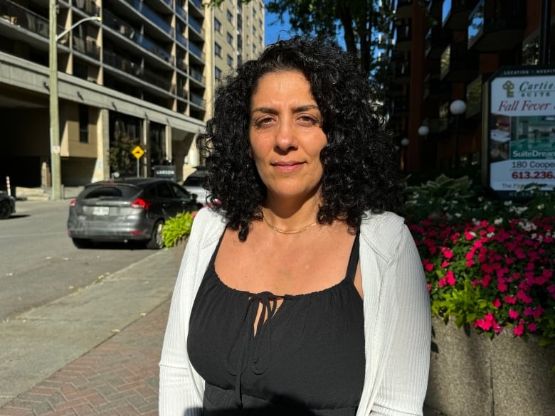 A woman poses for a photo on an urban street outdoors, next to some flowers.