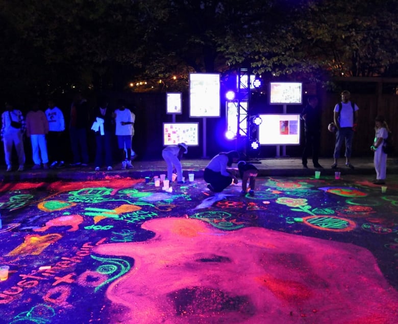 People kneel on the ground and use glow-in-the-dark chalk to make colourful designs at night. 