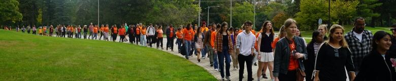 A group of people walk along a brick sidewalk. Many are dressed in orange shirts. 