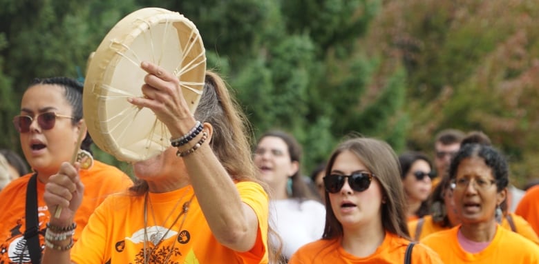 A group of people chant and hit drums with a line of people behind them.