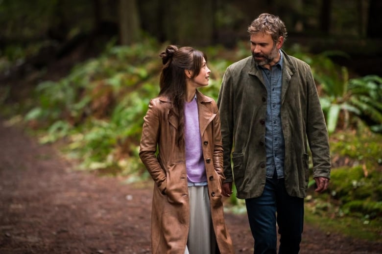 two people walk together through a coastal forest