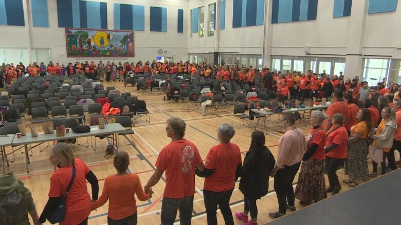 People wearing orange shirts, holding hands and standing in a circle. 