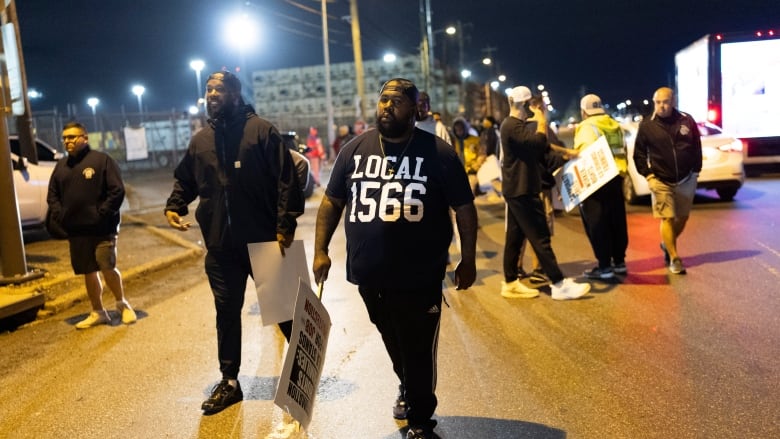 Men walk on a street carrying picket signs.