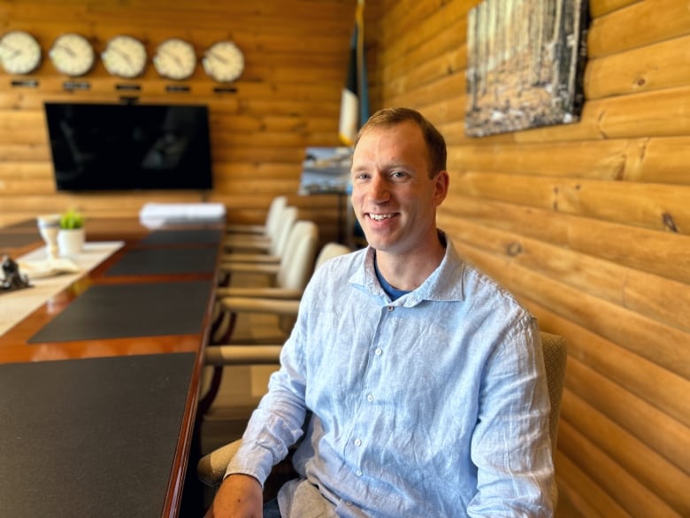 Man sitting in conference room with wood-panelled walls, smiling at camera