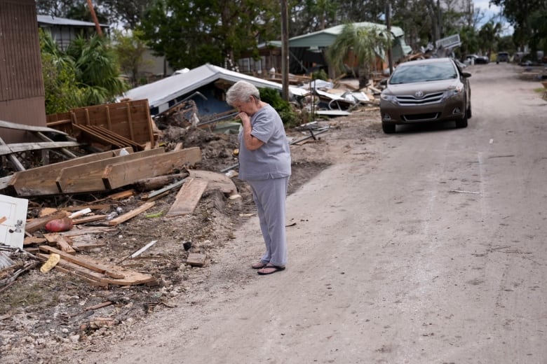 Woman with hand over mouth while looking at debris from destroyed house