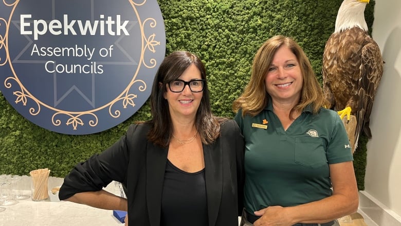 Two women standing in front of Epekwitk sign and bald eagle ornament.