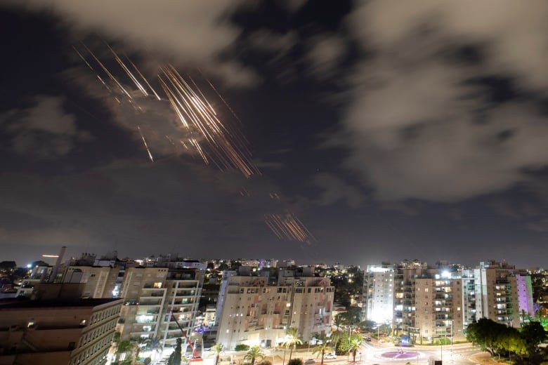 Missiles are seen flying over a city in a night sky. 