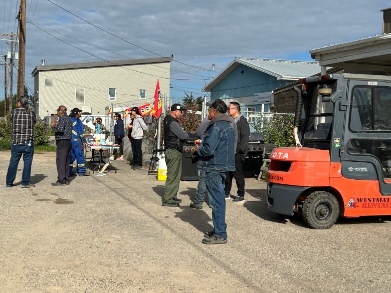 Workers milling about and shaking hands, with table set up and flags.