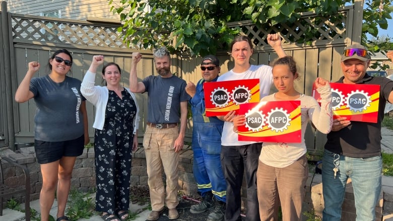 Seven workers with their fists up and holding signs that say PSAC.