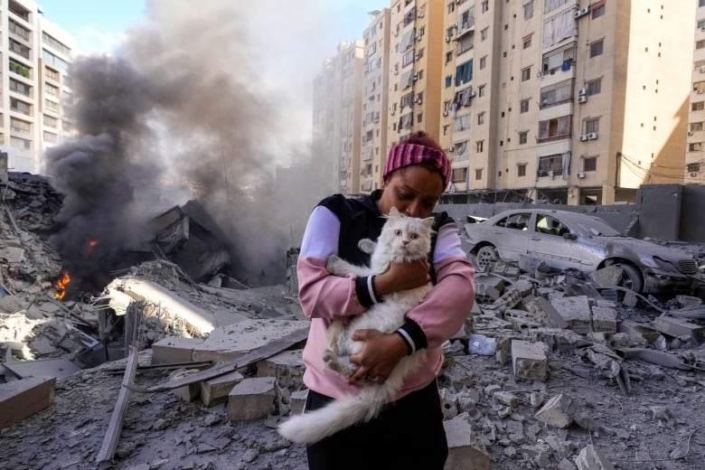 A woman holds her scared white cat in front of a destroyed building at the site of an Israeli airstrike 