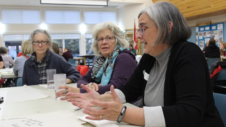 Three women in the midst of a discussion at a table. 