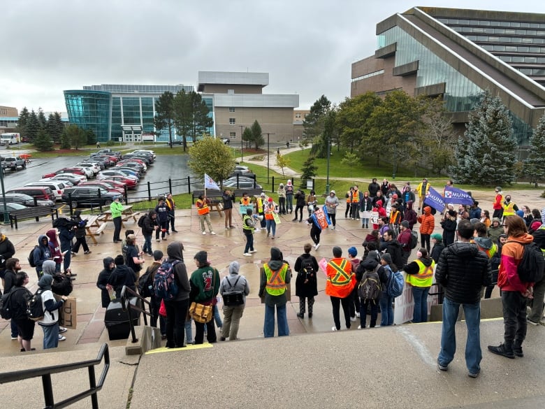 A crowd of people stand in an outdoor area of a university campus.