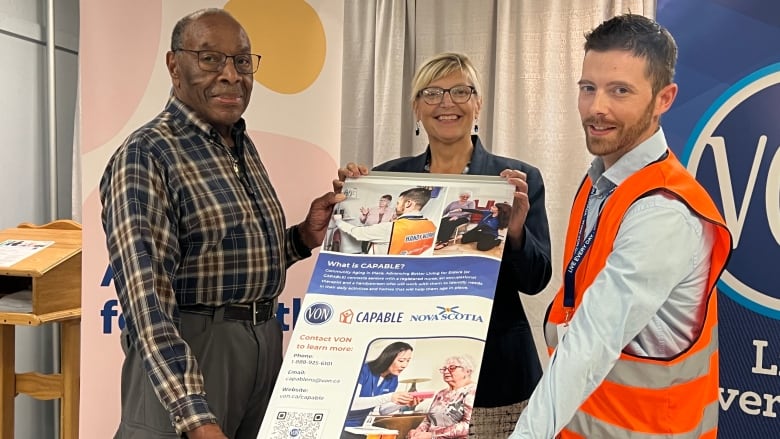 Two men stand on opposite sides of a poster. They hold the sides of the poster and a woman holds the top.