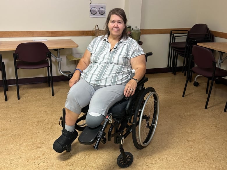 Woman with brown hair using a wheelchair is in a large room with tables and chairs in the background. 