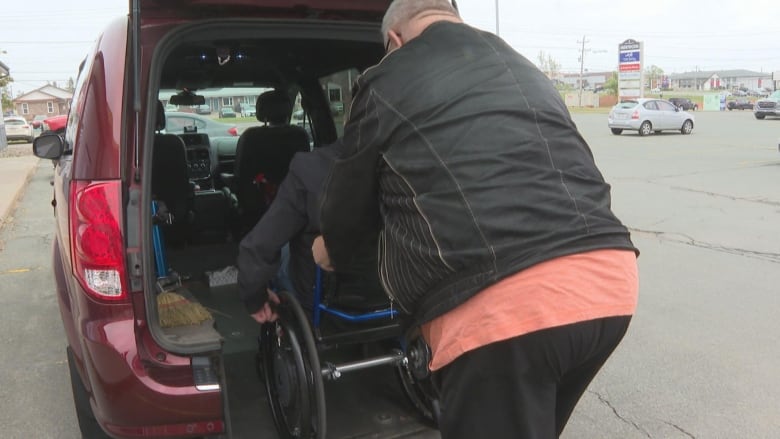 A person is pushing another person in a wheelchair into a taxi.