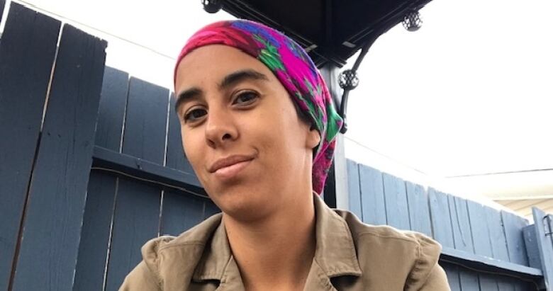 A woman in a headscarf smiles with a wooden fence in the background. 