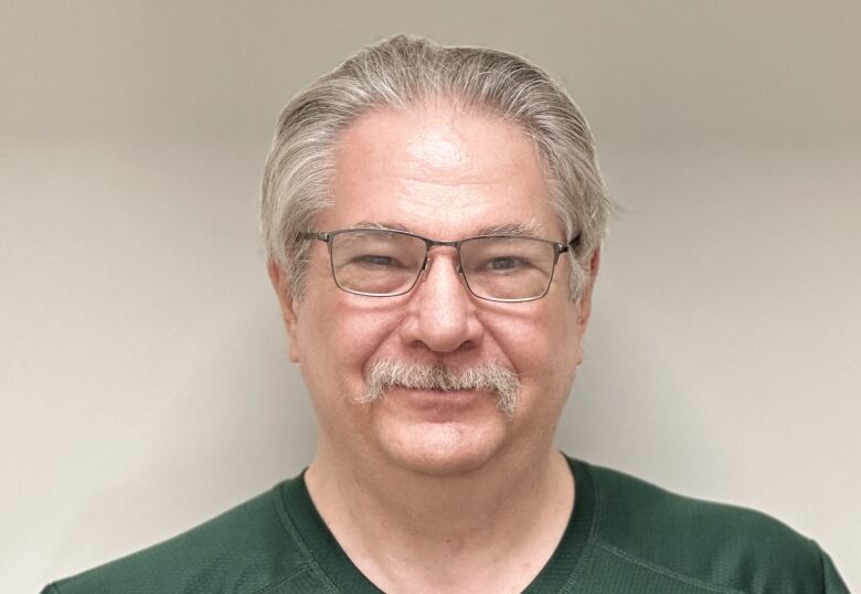 A man with grey hair and glasses smiles. 