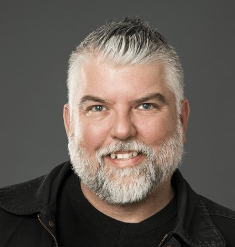 A man with a beard and white hair smiles. 