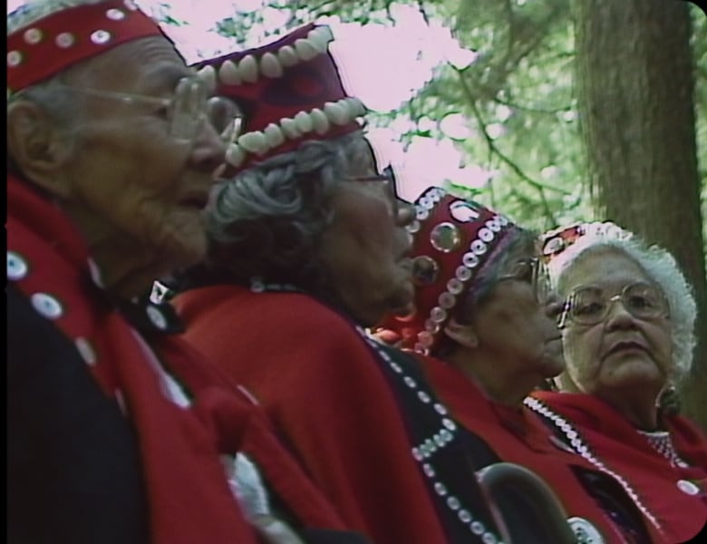 A group of older women wearing red regalia.