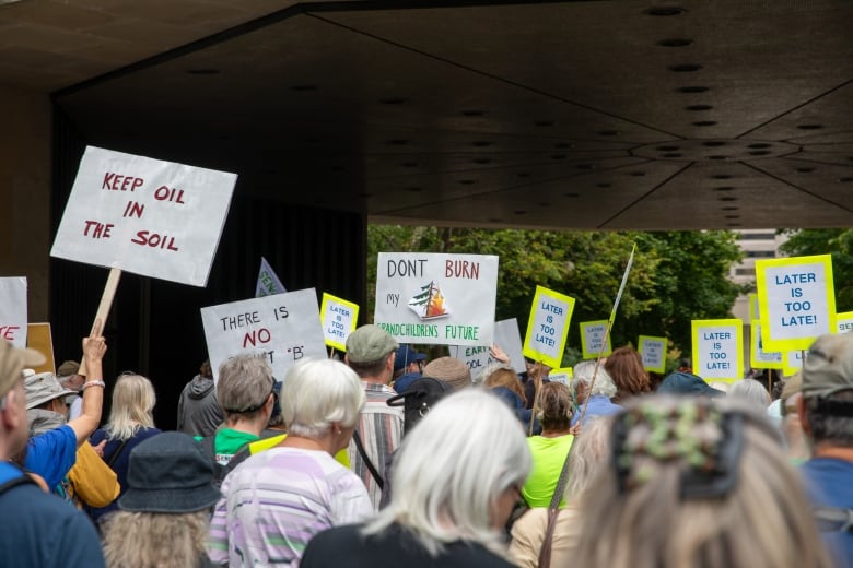 Crowd of protesters, many with grey hair, holding signs such as 'Later is two late'