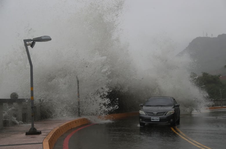 A car drives under a massive sea spray from the ocean