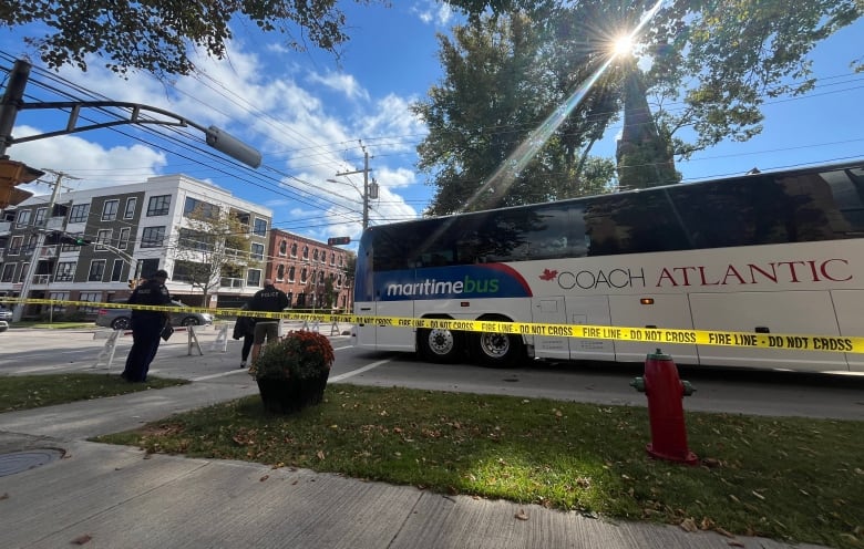 A motorcoach with a Maritime Bus/Coach Atlantic insignia behind yellow police tape sits at a city intersection.