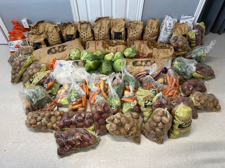 A large of amount of vegetables sit in bags on a floor.