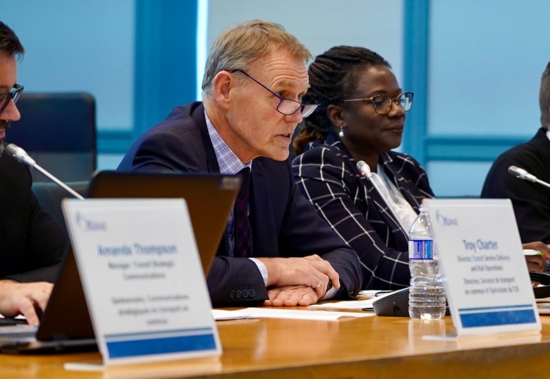 A man sits at a table and speaks into a microphone while a woman sits beside him.