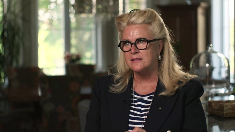 Woman wearing black glasses, striped shirt and black blazer speaks while seated