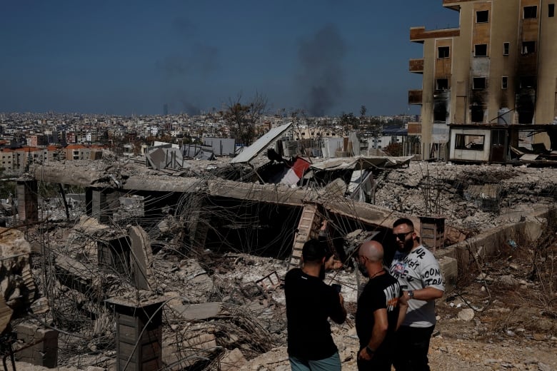 Three men stand amid the rubble of a destroyed building in Beirut.