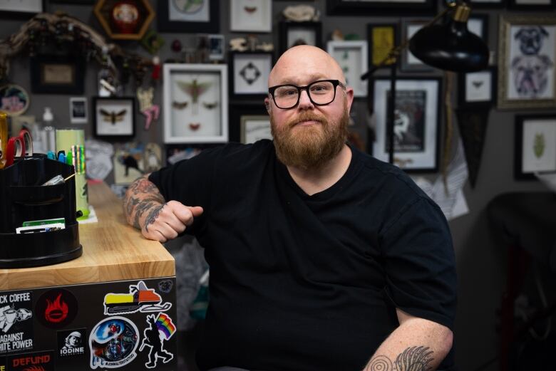 A man sits at a desk with a lot of art on the wall behind him.