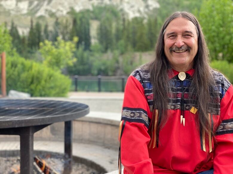 A man sits next to a fire pit by a river.