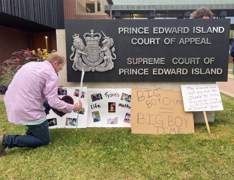 A sets up another sign memorializing Tyson MacDonald at the foot of the sign for the Supreme Court of Prince Edward Island.