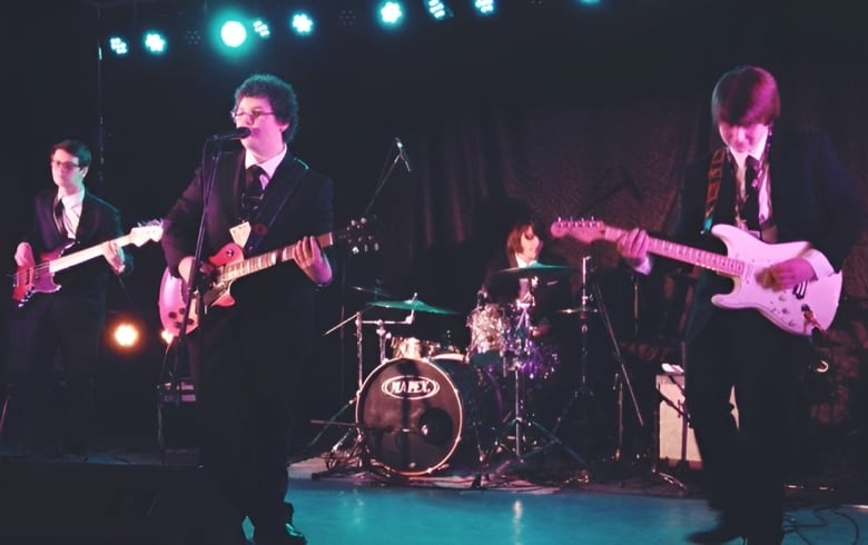 four teenagers in suits playing instruments in a stage.