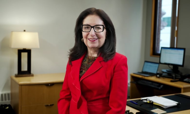 A woman with dark hair wearing a red blazer smiles for a photo in her office.